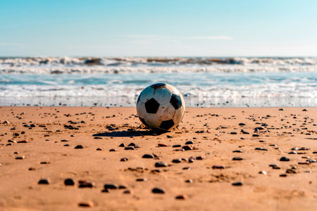 Worn soccer ball on the sandy beach after the game, the ball is dirty with sand on the shore of the beach with the sea in the backgroundの写真素材