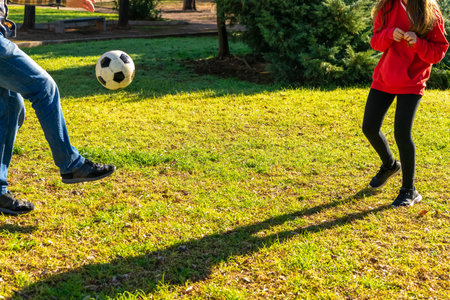 Legs of father and daughter playing soccer on the grass of a nice park on a sunny winter day. Fun concept.の写真素材