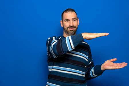Hispanic man with a beard dressed in a striped sweater making the gesture of holding something with...