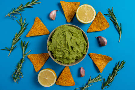 Composition of guacamole with the ingredients for its creation and the nachos for its consumption on a blue background.の写真素材