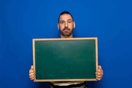 Spanish bearded man holding a blackboard isolated on blue studio background. Learning and messaging conceptの写真素材