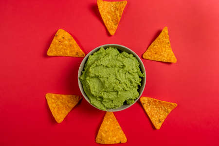 Top view of a ceramic bowl filled with the succulent guacamole sauce of Mexican origin on a red background.の写真素材