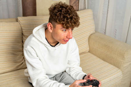 Portrait of attractive dark-haired Caucasian man, holding joystick and playing video games on TV on...