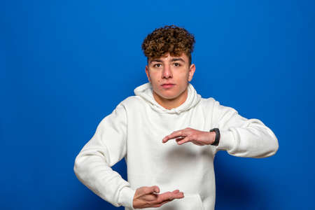 Young latin man against a blue background isolated holding something with both hands, product presentation.の写真素材