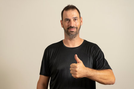 Handsome man wearing casual blue t-shirt standing over isolated beige background doing thumbs up...