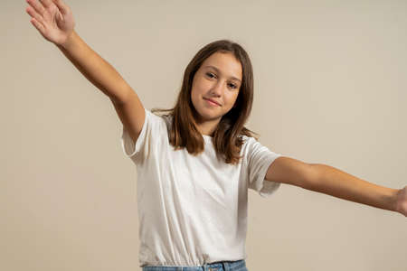 Pretty spanish teenage girl with brunette hair making the gesture of hugging someone while smiling at the camera, isolated over beige background.の写真素材