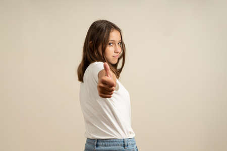 Photo of funny brunette teenage girl pointing at camera in white t-shirt isolated on beige background.の写真素材