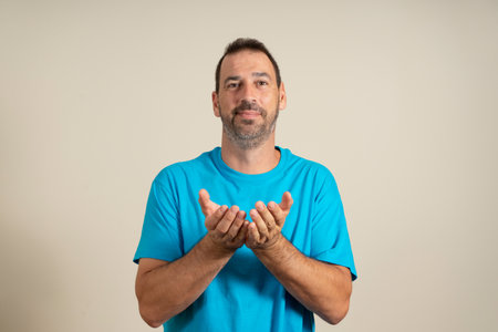 Latin bearded man in his 40s wearing a blue t-shirt offering something in his joined hands isolated...