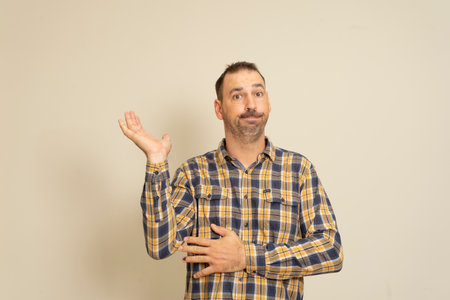 Hispanic man with beard and plaid shirt in skeptical attitude offering something in the palm of his...