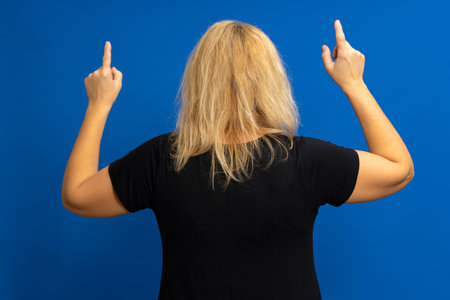 Caucasian blonde in a black T-shirt turned from behind and pointed with her index fingers, isolated...