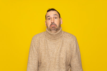 Bearded latino man doubting and shrugging, concept of indecision and insecurity, uncertain about something. Isolated on orange studio background.の写真素材