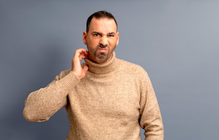 Middle age bearded man scratching himself highlighted with red collar on gray studio background, copy space. Upset man suffering from itchy, rash on his neck. Allergic reaction, eczema concept.の写真素材