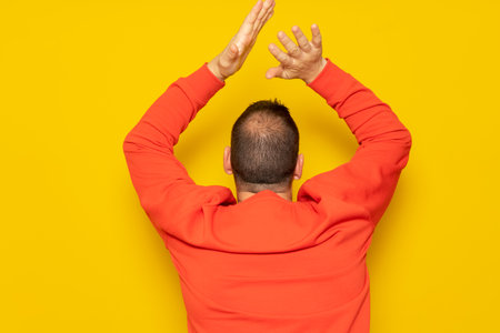 Half-bald man energetically clapping his back, he is excited about the spectacle he has just witnessed. Isolated on yellow background.の写真素材