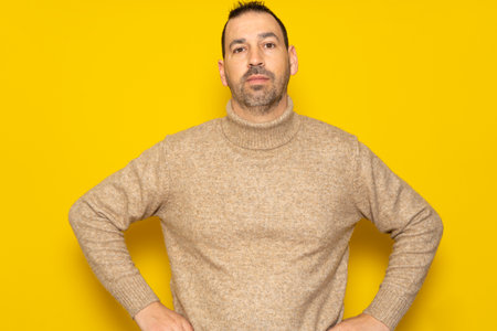 Cheerful bearded man wearing a red sweater posing isolated on gray background, studio portrait. People lifestyle concept. Mock up copy space. Standing with arms akimbo on waist blinking.の写真素材