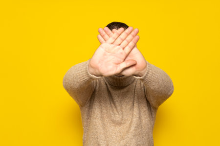 Hispanic man standing over yellow background rejection expression crossing his arms and palms making a negative signの写真素材