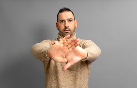 Hispanic man standing over yellow background rejection expression crossing his arms and palms making a negative sign.の写真素材