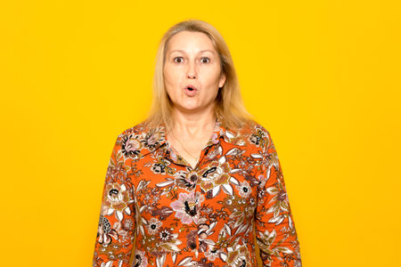 Caucasian woman in casual clothing scared and amazed with her mouth open in surprise, disbelief face. Isolated on yellow studio background.の写真素材