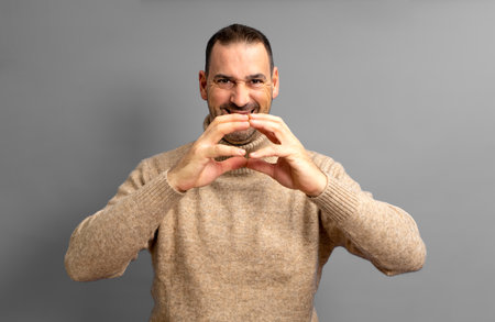 Hispanic man with a beard with the tips of his fingers together in an expression of evil, cunning and cold man plans a crime. Isolated on gray background.の写真素材