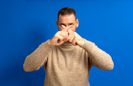 Hispanic man in his 40s crossing his fingers in stop and protest against the total oppression of the elites towards the proletariat, isolated on blue background.の写真素材
