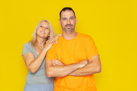 Caucasian real couple in their 40s posing happily, the man has his arms crossed and smiles as the...