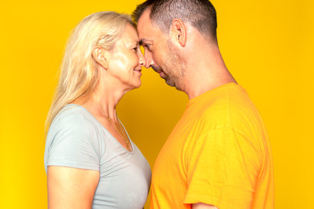 Romantic caucasian couple in their 40s happy touching foreheads and looking into each other's eyes, isolated over yellow studio backgroundの写真素材