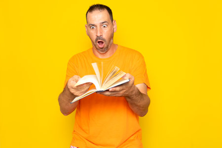 Bearded Hispanic man in his 40s turning the pages of a book visibly excited, isolated on yellow studio backgroundの写真素材