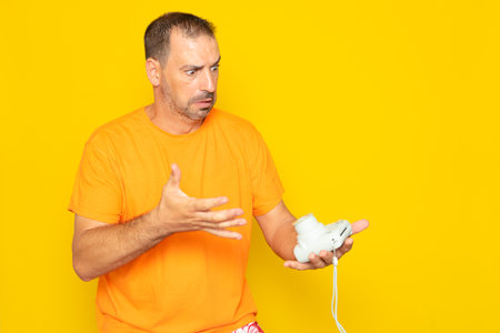 Hispanic man with beard in his 40s frustrated and angry for not understanding the operation of an instant camera, isolated on yellow studio background.の写真素材