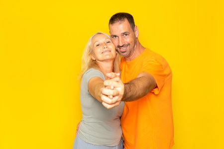 Caucasian married couple dancing a tango with hands stretched and faces together, isolated on yellow studio backgroundの写真素材