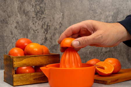 Mans hand squeezing an orange in a juicer with some ripe oranges in a still life with gray background, healthy living concept. Superfood rich in vitamin C.の写真素材