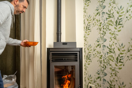 Man filling a pellet stove. Stove placed in the living room of the house. Sustainable future home heating concept.の写真素材