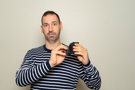 Bearded hispanic man in his 40s wearing a striped sweater searching for some cash in his empty...