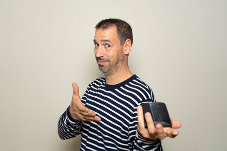Bearded hispanic man in his 40s wearing a ryas sweater happily and proudly offering his wallet full of money, isolated over beige backgroundの写真素材