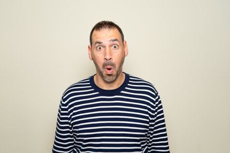 Hispanic man with beard about 40s scared and shocked with surprise expression, fear and excited face. Isolated on beige background.の写真素材