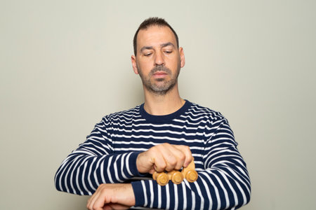 Bearded hispanic man in his 40s wearing a striped sweater running a wooden massager over his sore arm, isolated on beige studio backgroundの写真素材