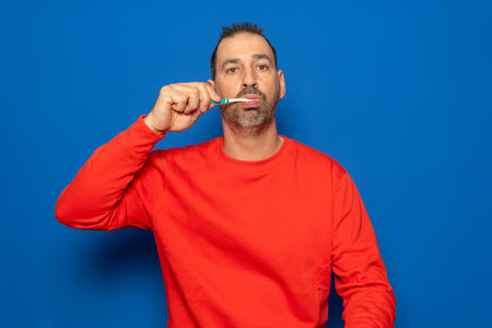 Bearded hispanic man in his 40s brushing his teeth with a toothbrush, cleaning teeth and tongue as a healthy morning health care routine.の写真素材