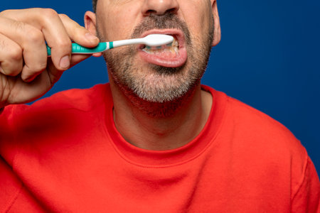 Close up of bearded hispanic man in his 40s brushing his teeth, isolated on blue studio background. Dental hygiene and health conceptの写真素材