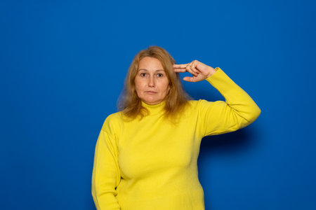 Beautiful caucasian woman about 40s wearing yellow sweater over isolated blue background. Pointing with hand and fingers to headの写真素材