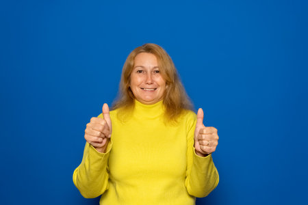 Caucasian woman about 40s wearing yellow sweater putting her thumbs up, agrees with something, gives...