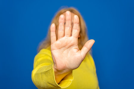 Hand gesture with woman in studio on blue background. Palm and gesture for protection or self-defenseの写真素材