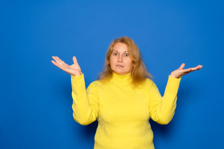 Maybe I have no idea. Portrait of a confused woman shrugging her shoulders in bewilderment, hesitating and unsure, not knowing the answer. Isolated on a blue background.の写真素材