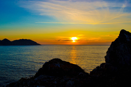 Amazing and colorful sunset over the sea with dark rocks at the front. Beautiful reflection in the waterの写真素材