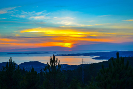 Amazing and colorful sunset over the sea with dark trees at the front. Beautiful reflection in the waterの写真素材