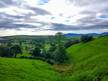 View of a green grass valley around the mountains with a cloudy sky. Camino de Santiago primitivoの写真素材