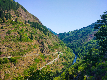 Meadow of a road in middle of a hillside of a mountain with a river crossing the valleyの写真素材