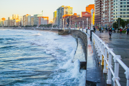 Waves splashing against the wall in San Lorenzo beach in Gijon, Asturias, Spain, with the promenade and buildings in one sideのeditorial素材