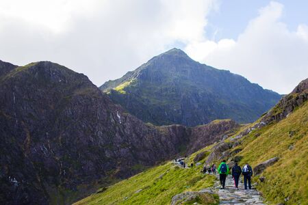 People walking to the summit of a mountain through a pathway surrounded by beautiful landscapes in Snowdonia, Walesの写真素材