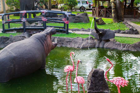 Traditional african handcrafted wooden statues of hipo, elephant and flamingo in a pond of the garden of Cultural Heritage store in Arusha, Tanzaniaのeditorial素材
