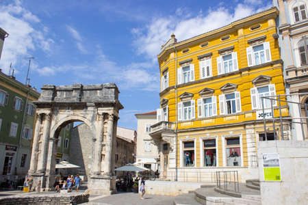 Pula, Croatia; 7/18/2019: Arch of the Sergii (Slavoluk Sergijevaca), an Ancient Roman triumphal arch located in Pula, with a yellow building close to itのeditorial素材
