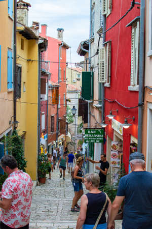 Rovinj, Croatia; 7/18/2019: Vertical photo of a picturesque narrow street with colorful facades of the houses and people walkingのeditorial素材