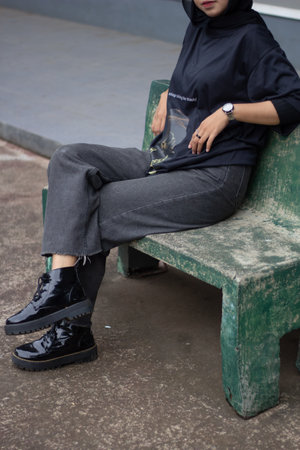 An Asian female model exudes a relaxed style, donning jeans and a black shirt while seated on a...